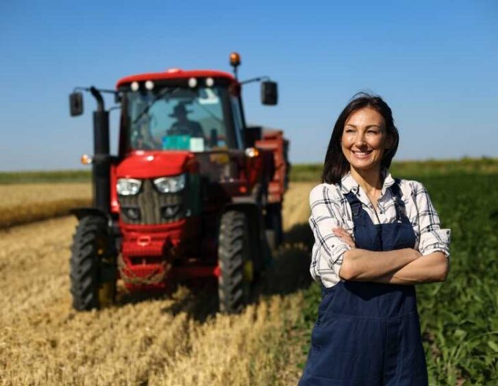 A woman in overalls standing in front of a tractor in a field. A Woman In Overalls Standing In Front Of A Tractor In A Field.