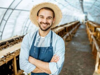 A Man In A Straw Hat Standing In A Greenhouse With Bees.
